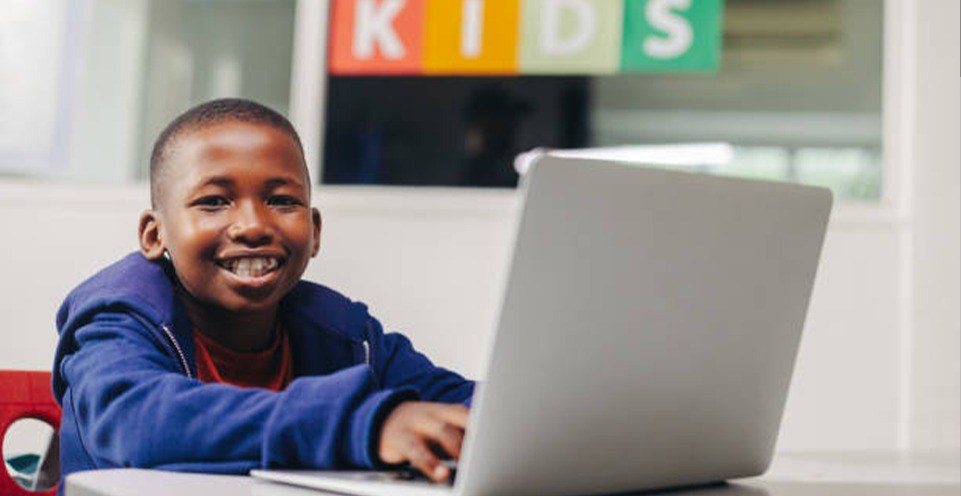 Un garçon souriant travaille sur son ordinateur portable